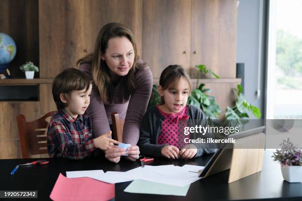 children and mother doing origami toys using colored papers by following the steps instructed in the video tutorial on digital tablet - origami spiel stock-fotos und bilder