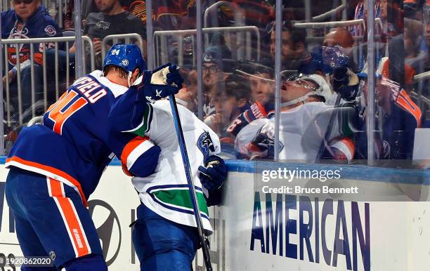 Scott Mayfield of the New York Islanders checks Nils Hoglander of the Vancouver Canucks into the glass during the first period at UBS Arena on...