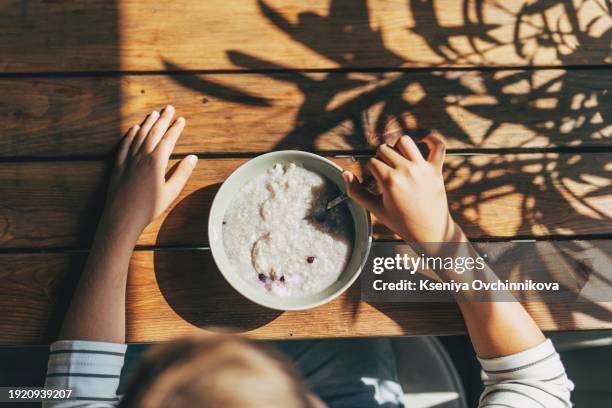 the boy has breakfast porridge sitting near the window - children eating breakfast at school stock pictures, royalty-free photos & images