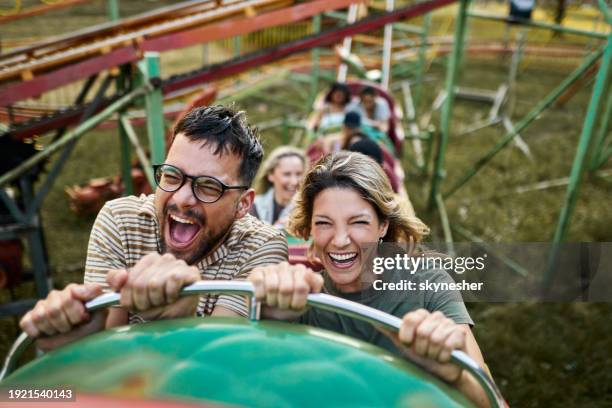 cheerful couple riding on rollercoaster at amusement park. - parque de diversões edifício de entretenimento - fotografias e filmes do acervo