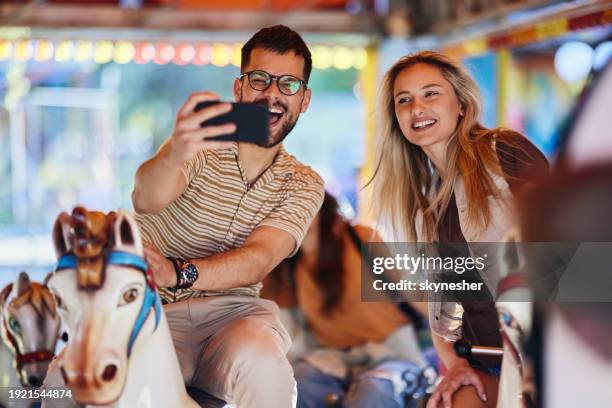 happy couple taking a selfie during carousel ride at amusement park. - mammal stock-fotos und bilder