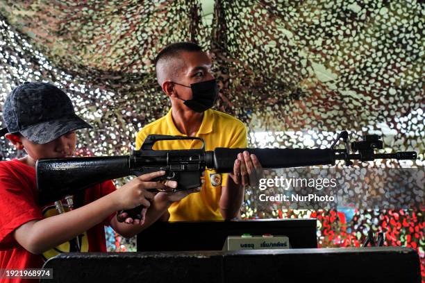 Thai child is aiming with a military gun with the assistance of a soldier during National Children's Day inside a military base in Bangkok, Thailand,...