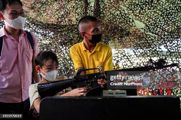 Thai child is aiming with a military gun with the assistance of a soldier during National Children's Day inside a military base in Bangkok, Thailand,...