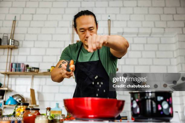 handsome chinese chef puts spices in frying pan - korean ethnicity stock pictures, royalty-free photos & images