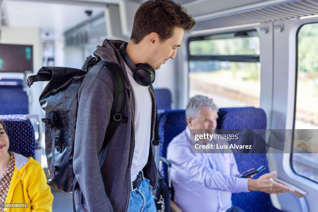 Young man on train with a senior man showing him a seat