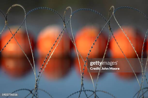 Coils of razor wire installed by Texas National Guard soldiers as well as a floating barrier ordered by Texas Governor Greg Abbott lie along the Rio...