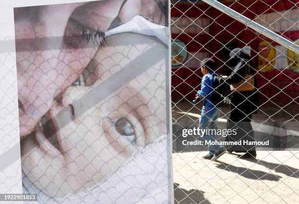 Woman and her son walk near a billboard bearing the image of a Palestinian mother crying over her daughter killed in an aerial attack carried out by...