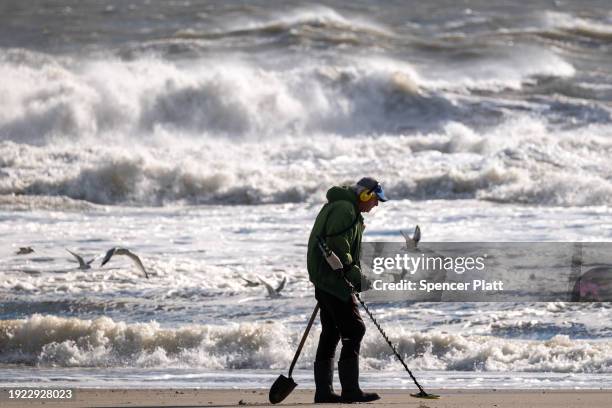 Man uses a metal detector along the beach at Rockaway during heavy surf following a storm that brought high winds and rain to the area on January 10,...