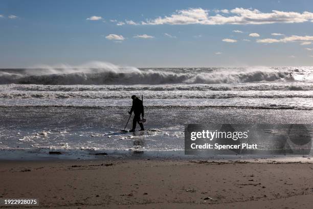 Man uses a metal detector along the beach at Rockaway during heavy surf following a storm that brought high winds and rain to the area on January 10,...