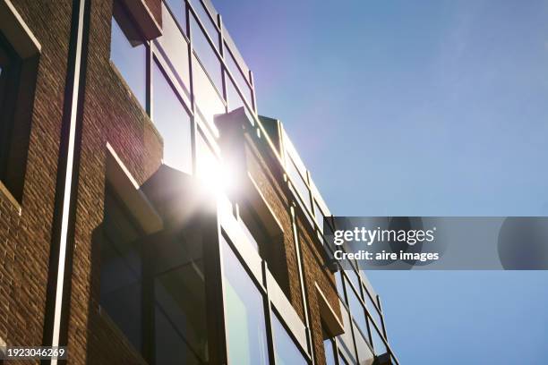a large building with brick walls and glass windows, sunlight is reflecting off one of them, with a clear blue sky. - amsterdam blue sky stock-fotos und bilder