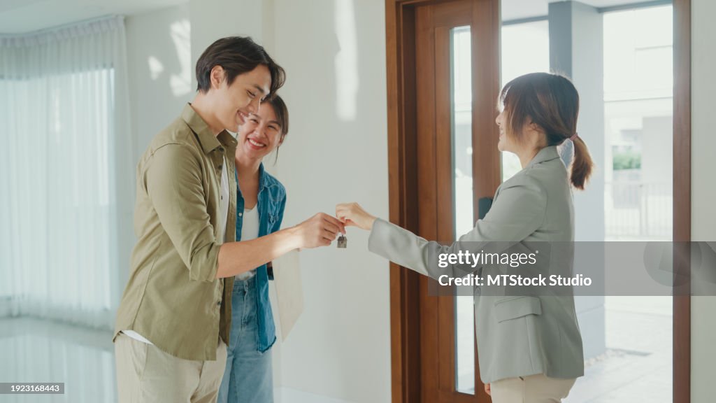 Young Asian woman real estate broker giving house keys to client after signing agreement contract. Buying a new house.
