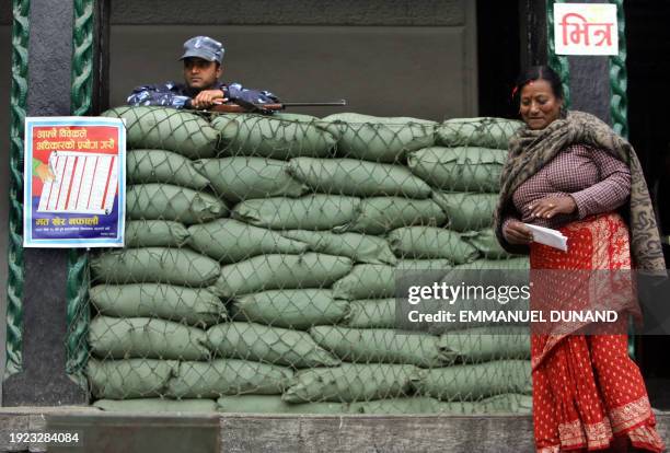 Nepalese voter walks out, ballot in hand, of a polling booth set up behind army sand bags under the close watch of an armed Nepalese policeman during...