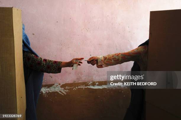 Burqa-clad Afghan woman hands another a pen as they cast their votes at a polling station in Mazar-e-Sharif on August 20 during voting for...