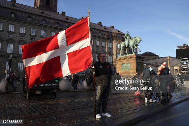 Man holds a flag of Denmark in Christiansborg Palace square on January 14, 2024 in Copenhagen, Denmark. Crown Prince Frederik will succeed Queen...