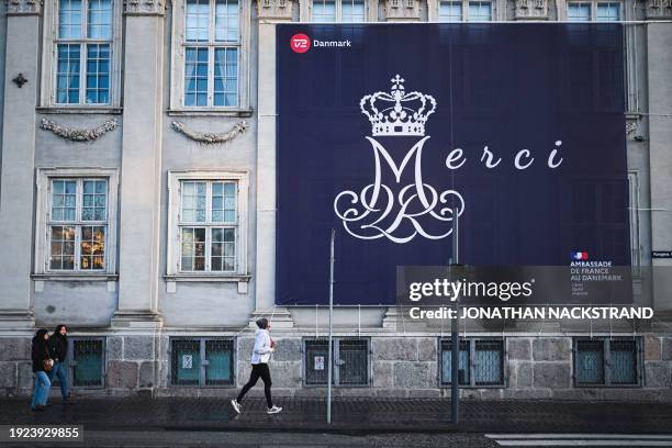 Man runs by a huge placard reading "Merci" and hanging on the facade of the French embassy ahead of the proclamation of abdication of Denmark's Queen...