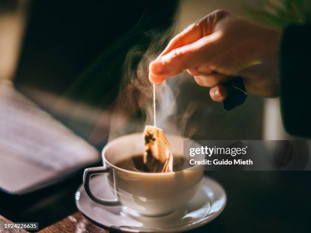 hand is picking a tea bag out of a white cup. - tea bag stock pictures, royalty-free photos & images