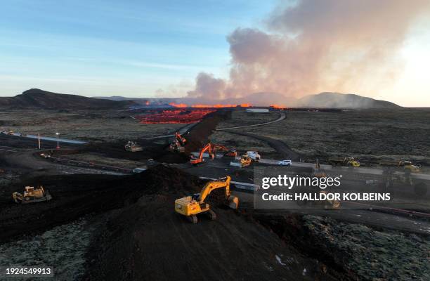 Aerial view taken on January 14, 2024 shows emergency personnel using diggers to build a protective wall trying to prevent flowing lava to reach the...