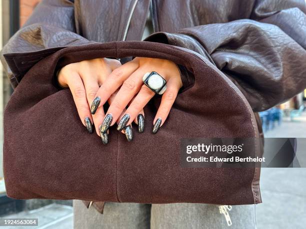 Samia Laaboudi wears a cocoa suede mini tote bag, a finger ring, black and white shiny / glitter nail polish, during a remote street style fashion...
