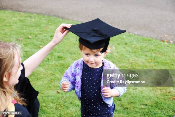 young mum playfully putting her mortarboard hat on her young daughter after she received her masters degree. - cute college girl stock pictures, royalty-free photos & images