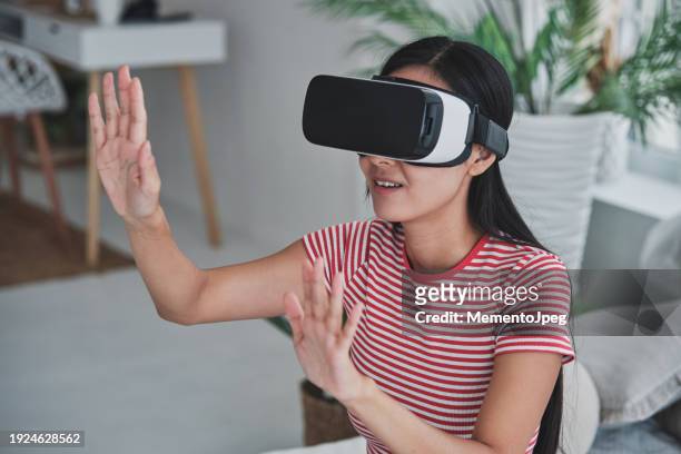 asian woman using virtual reality headset at home, girl wearing vr goggles touching air with hands, watching 3d video, shopping in metaverse. people and innovative future technologies - virtual stock pictures, royalty-free photos & images