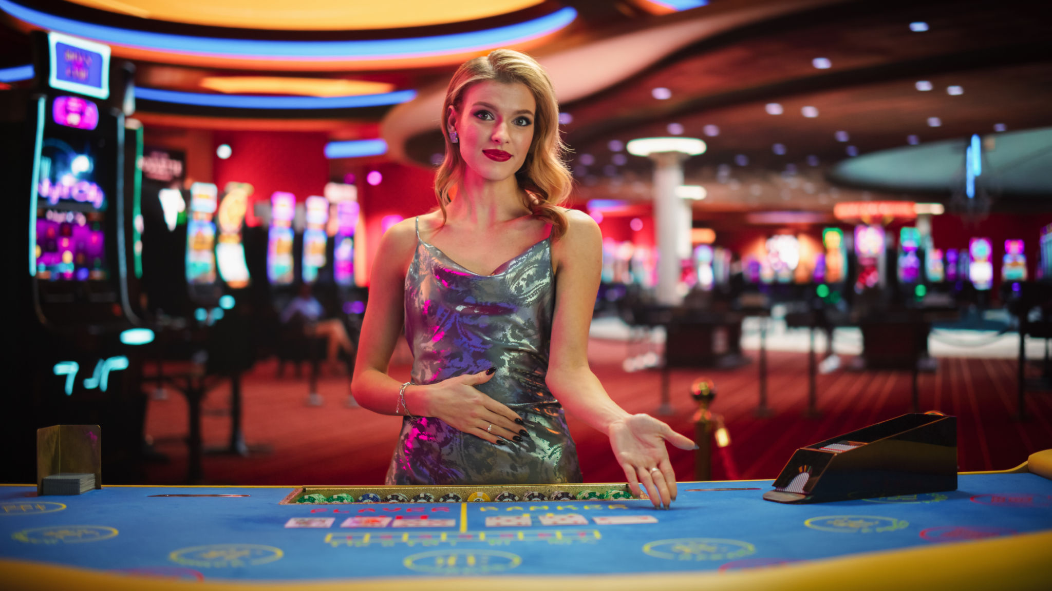 Beautiful Caucasian Woman Working As A Dealer At Classy Casino. Professional Female Baccarat Croupier In a Fancy Silver Dress, Presenting Playing Cards, Looking At Camera And Smiling Beautiful Caucasian Woman Working As A Dealer At Classy Casino. Professional Female Baccarat Croupier In a Fancy Silver Dress, Presenting Playing Cards, Looking At Camera And Smiling