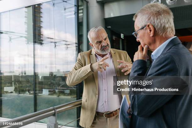 two business colleagues deep in conversation while standing in office foyer - deep conversation stock pictures, royalty-free photos & images