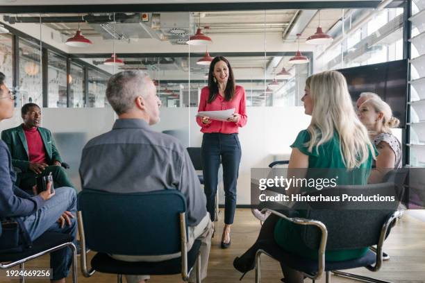businesswoman conducting meeting, reading in front of colleagues - mittig stock-fotos und bilder