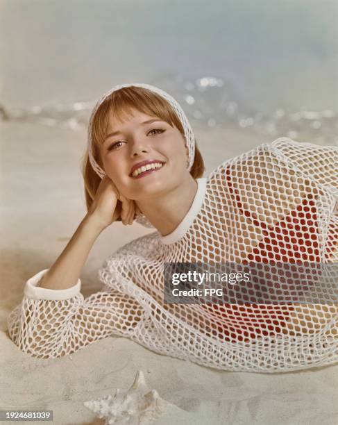 Fashion model wearing matching white mesh top and headband, and red bikini top, on a beach, US, 1998.
