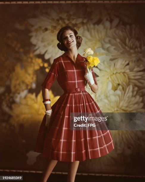 Fashion model wearing half sleeve check flared dress with matching check belt, and cream-coloured gloves, holds flowers on a Chrysanthemums...