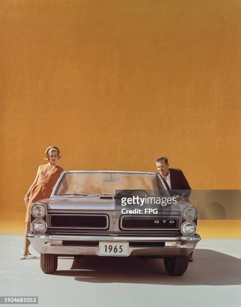 Woman and a man standing near a 1965 Pontiac GTO convertible, US, circa 1965.