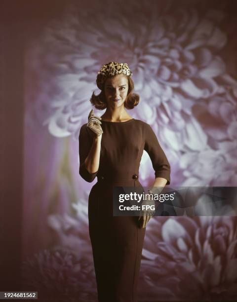 Fashion model wearing brown three quarter sleeve pencil dress, beige suede gloves, and cheetah fur beret, against a floral background, US, 1996.