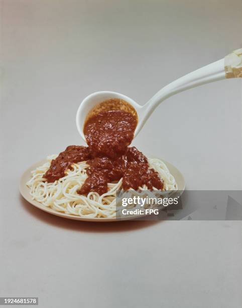 Ladle pouring tomato sauce on a plate of spaghetti, US, 1968.