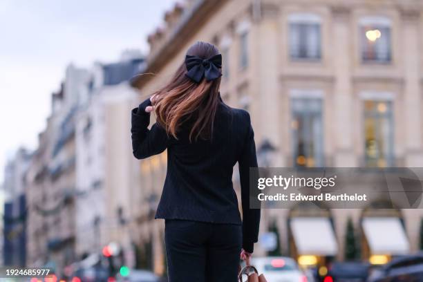 Amanda Derhy wears earrings, a bow hair clip, a black jacket, a brown leather bag, during a street style fashion photo session, on January 06, 2024...