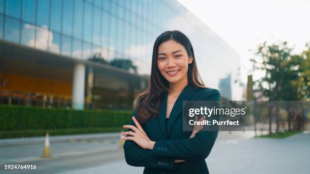 retrato de una joven empresaria asiática hermosa feliz en traje de negocios mirando a la cámara y sonriendo, directora ejecutiva confiada de pie y posando con los brazos cruzados, gerente femenina profesional que trabaja en un edificio de oficinas modern - director ejecutivo fotografías e imágenes de stock