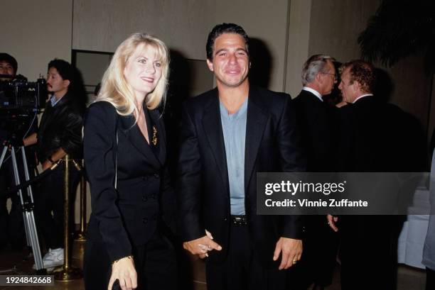 American actor Tony Danza, wearing a black suit over a grey t-shirt, holding hands with his wife, Tracy, who wears a black suit with a gold brooch on...