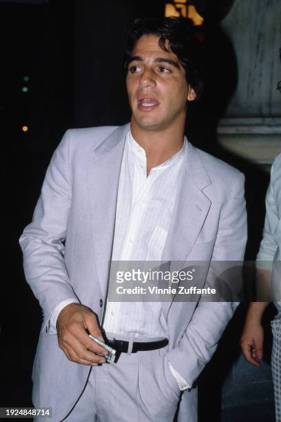 American actor Tony Danza, wearing a light grey suit over a white shirt, open at the collar, his left hand in his pocket, his right holding a folded...