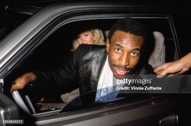 American football player Eric Dickerson wearing a black jacket with black leather trim over a white shirt, with a blonde woman sitting in the...