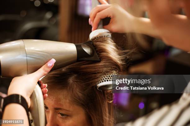 post-transformation elegance: a hairstylist expertly uses a hairdryer and comb to dry and style a client's hair following a stunning color and cut session, creating a final touch of elegance and sophistication. - frau haarsträhne blond beauty stock-fotos und bilder