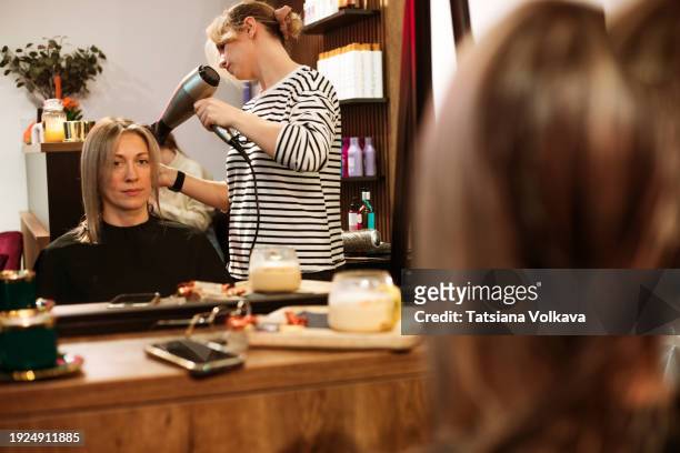 in a chic salon, a hairstylist works their magic with a hairdryer and comb, crafting a stunning haircut and vibrant hair coloring during a stylish styling session for a woman. - frau haarsträhne blond beauty stock-fotos und bilder