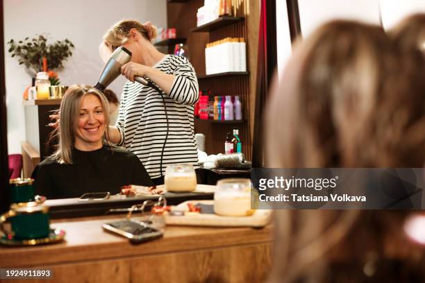 the hairstylist, exuding elegance, uses a hairdryer to craft sophistication in a woman's styling session. - frau haarsträhne blond beauty stock-fotos und bilder