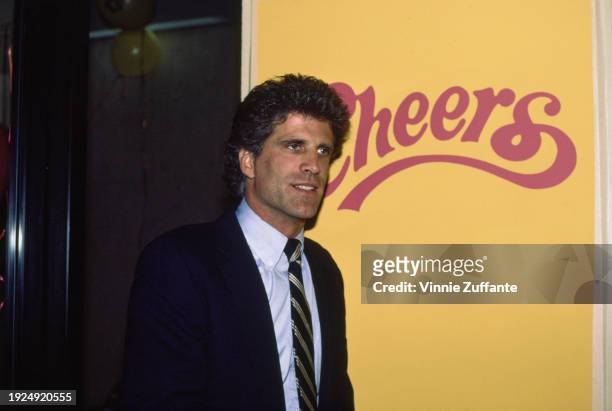 American actor Ted Danson wearing a dark blue blazer over a light blue shirt with a dark blue, white and red diagonally-striped tie, pointing to a...