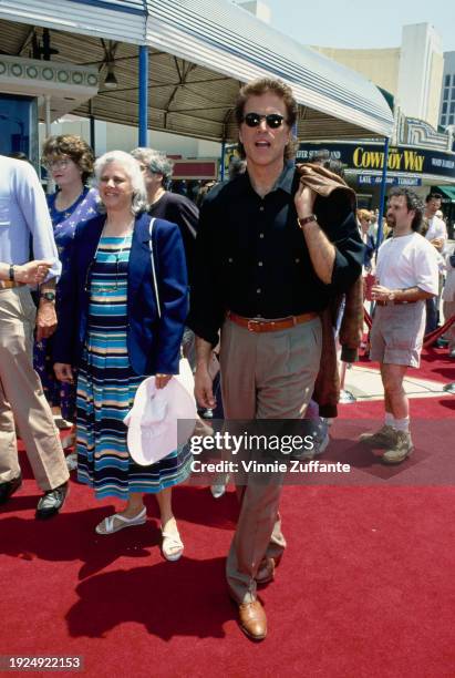 American actor Ted Danson, wearing a black shirt with beige trousers, and holding a brown leather jacket over his shoulder, attends the Westwood...