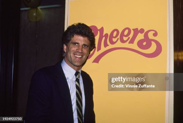 American actor Ted Danson wearing a dark blue blazer over a light blue shirt with a dark blue, white and red diagonally-striped tie, pointing to a...