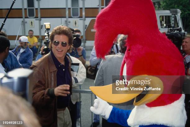 American actor Ted Danson, wearing a dark blue shirt under a brown leather jacket, with sunglasses, alongside a person in a Woody Woodpecker costume,...