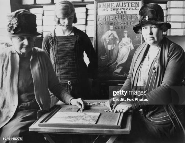 Anne Austen founder of the Jigsaw Puzzle Club of Knightsbridge and the Viscountess Ashbrook, Gladys Lucille Beatrice sitting at a table and working...