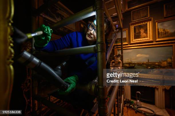 Conservator Tomasina Munden cleans and dusts a painting in the Picture Room from a scaffold during the Sir John Soane's Museum annual cleaning week...