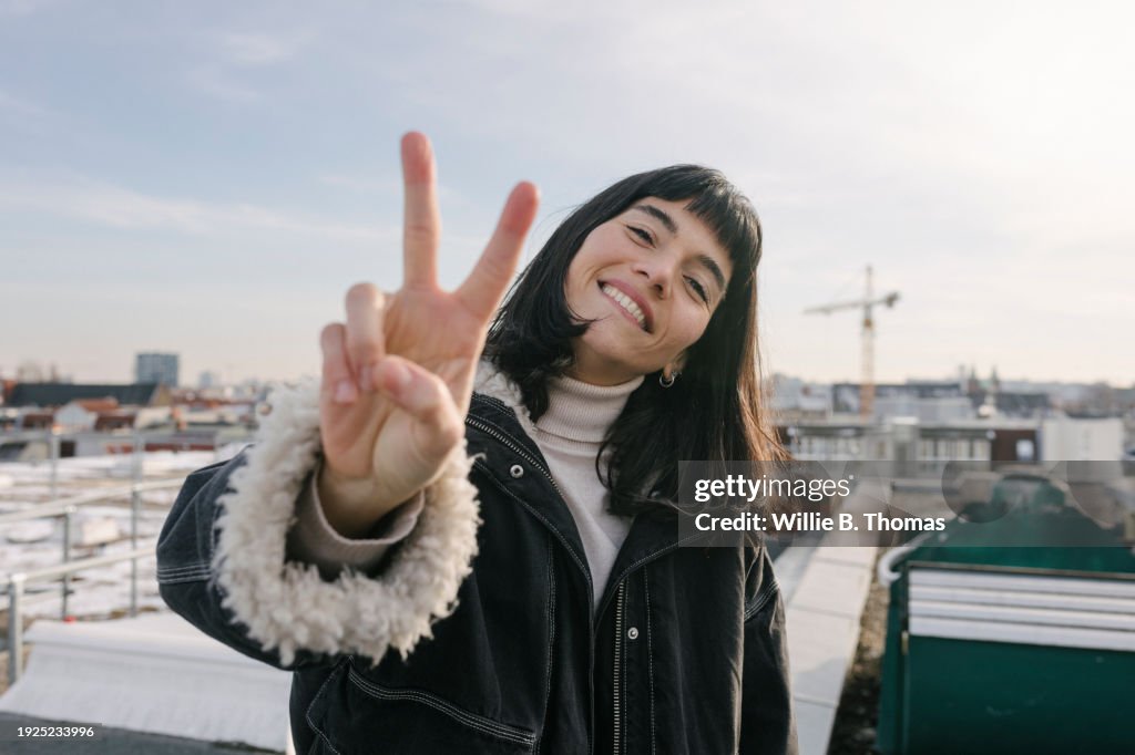 Portrait Of Woman Giving Peace Sign While Standing On Rooftop