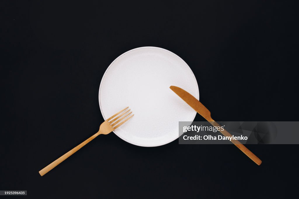 Empty plate, fork and knife on black background