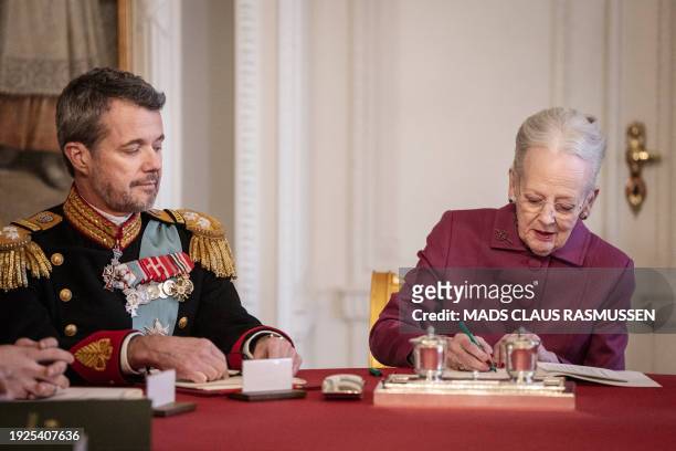 Queen Margrethe II of Denmark signs a declaration of abdication as King Frederik X of Denmark looks on in the Council of State at the Christiansborg...