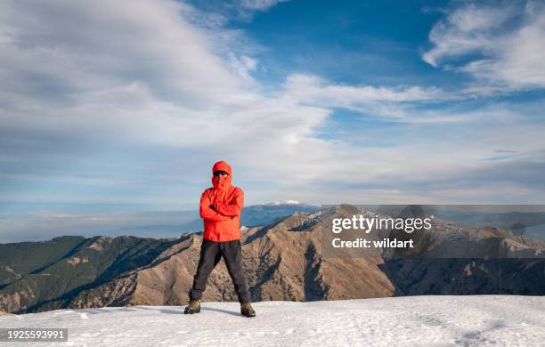 mountain climber is looking at the camera , arms crossed while standing on the summit of a high altitude mountain. - sport determination stock pictures, royalty-free photos & images